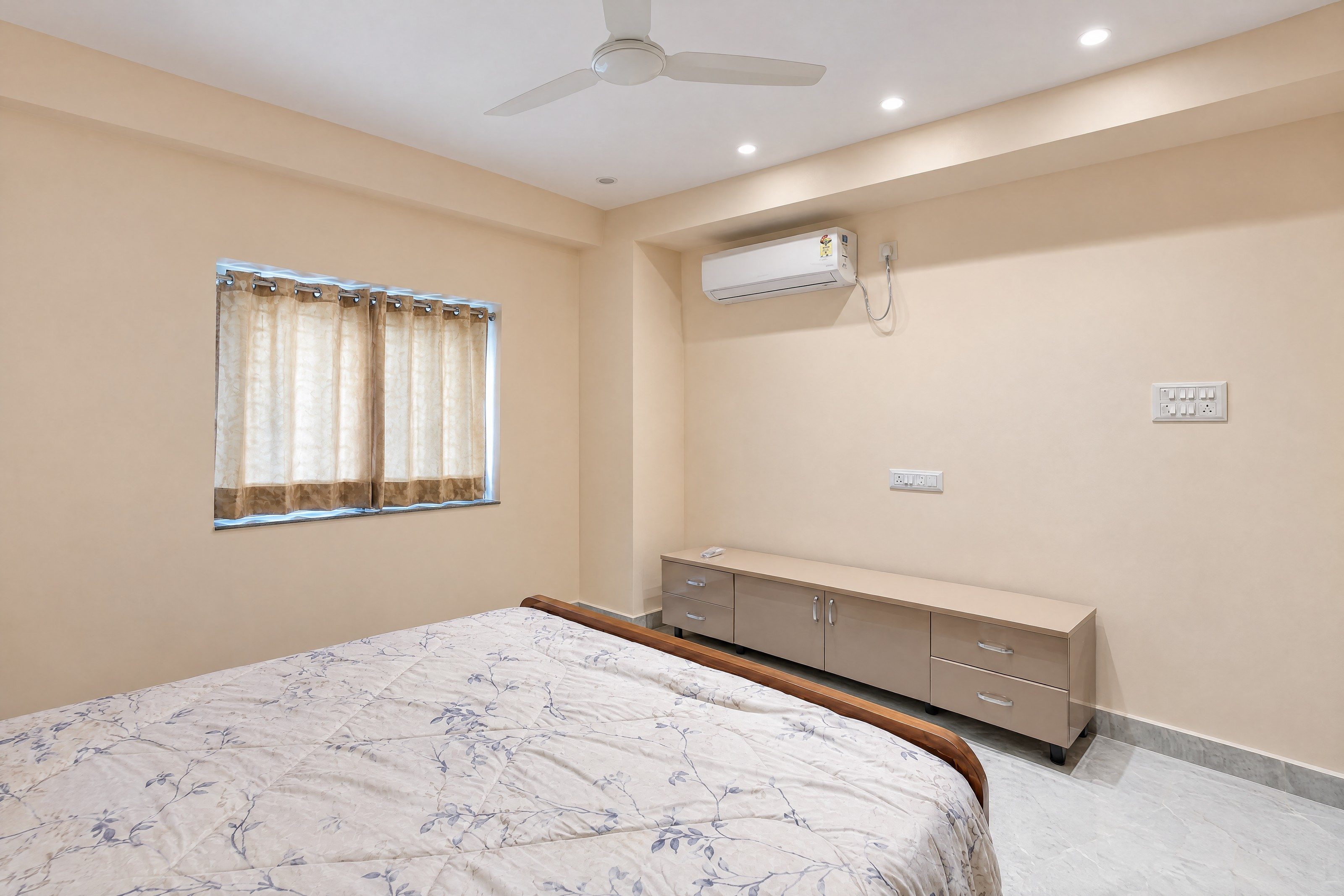 An AI re-angle of a bedroom as a level landscape frame from the corner of the room: the curtained window on one wall, the AC and the dresser on the other, the bed in the foreground, in even daylight.